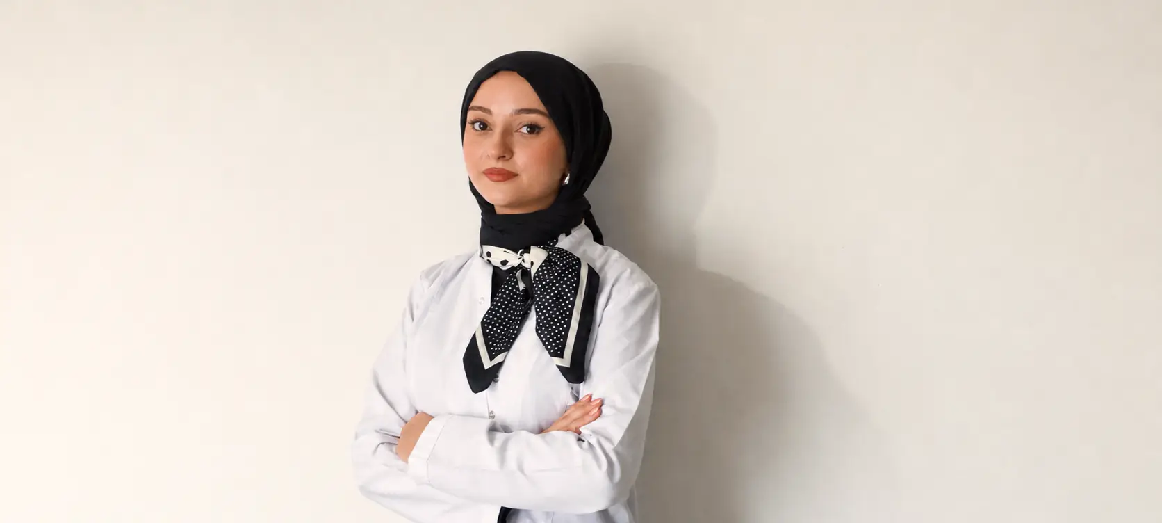 Diyetisyen Yaren Zorlu beyaz önlüğüyle, açık renk bir duvarın önünde