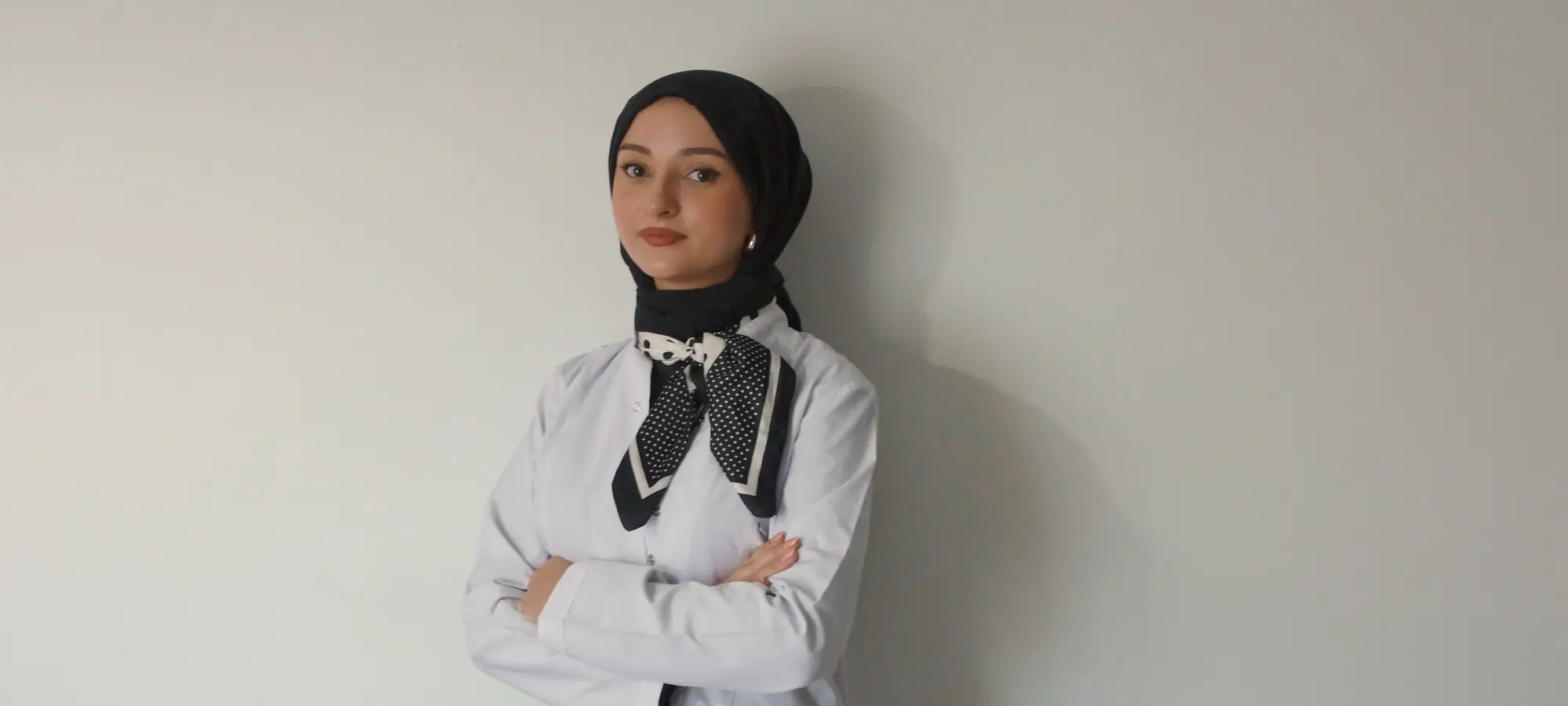 Diyetisyen Yaren Zorlu beyaz önlüğüyle, açık renk bir duvarın önünde