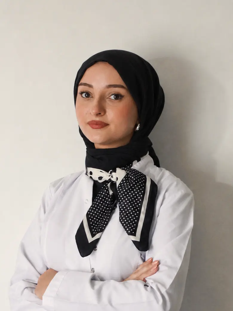 Diyetisyen Yaren Zorlu, beyaz önlüğü ve siyah başörtüsüyle kameraya bakıyor